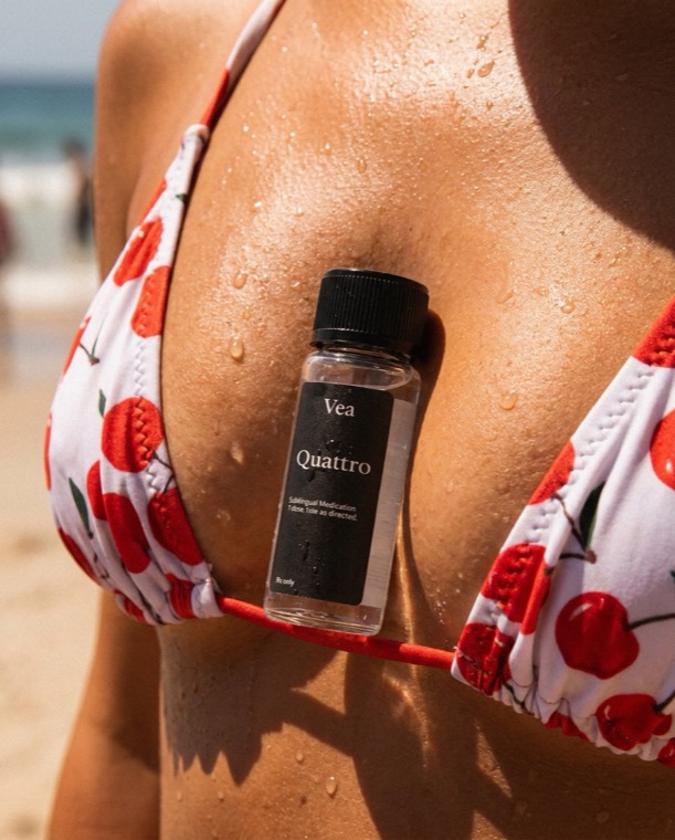 A bottle of Quattro by Vea Health tucked into a cherry-print bikini top at the beach